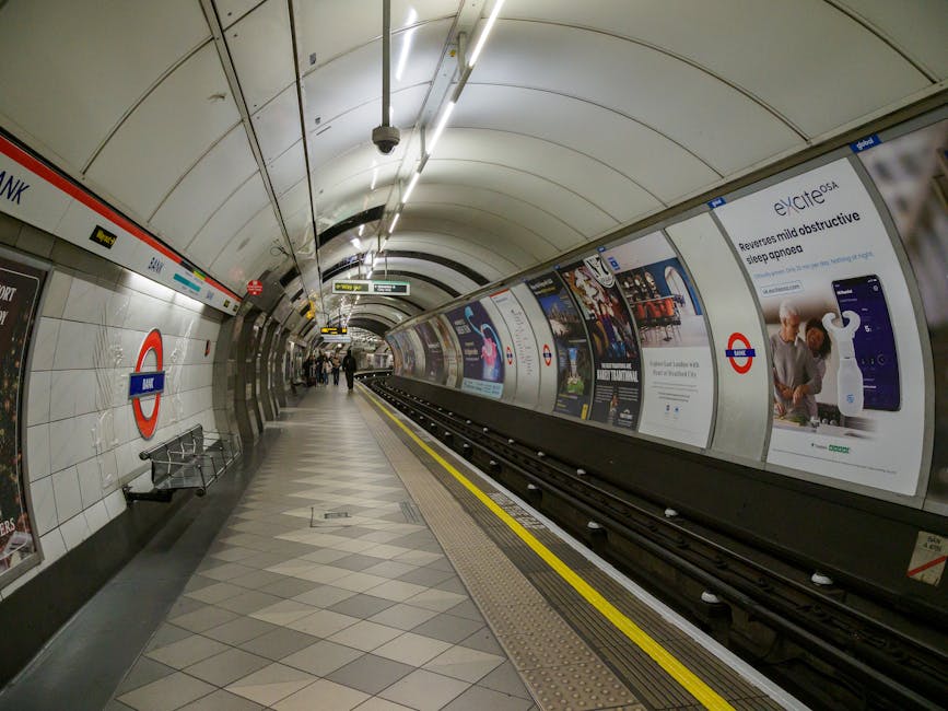 A photograph of a London Underground station platform at High Street Kensington, showing a yellowish-tinted train with closed doors parked alongside. The platform has a textured yellow safety strip ru